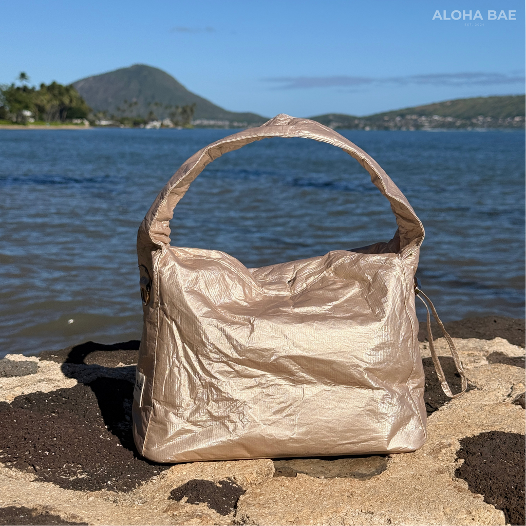 Aloha Bae champagne-colored hobo bag with a sleek, rounded shape and shoulder strap, featuring minimalistic design details.
