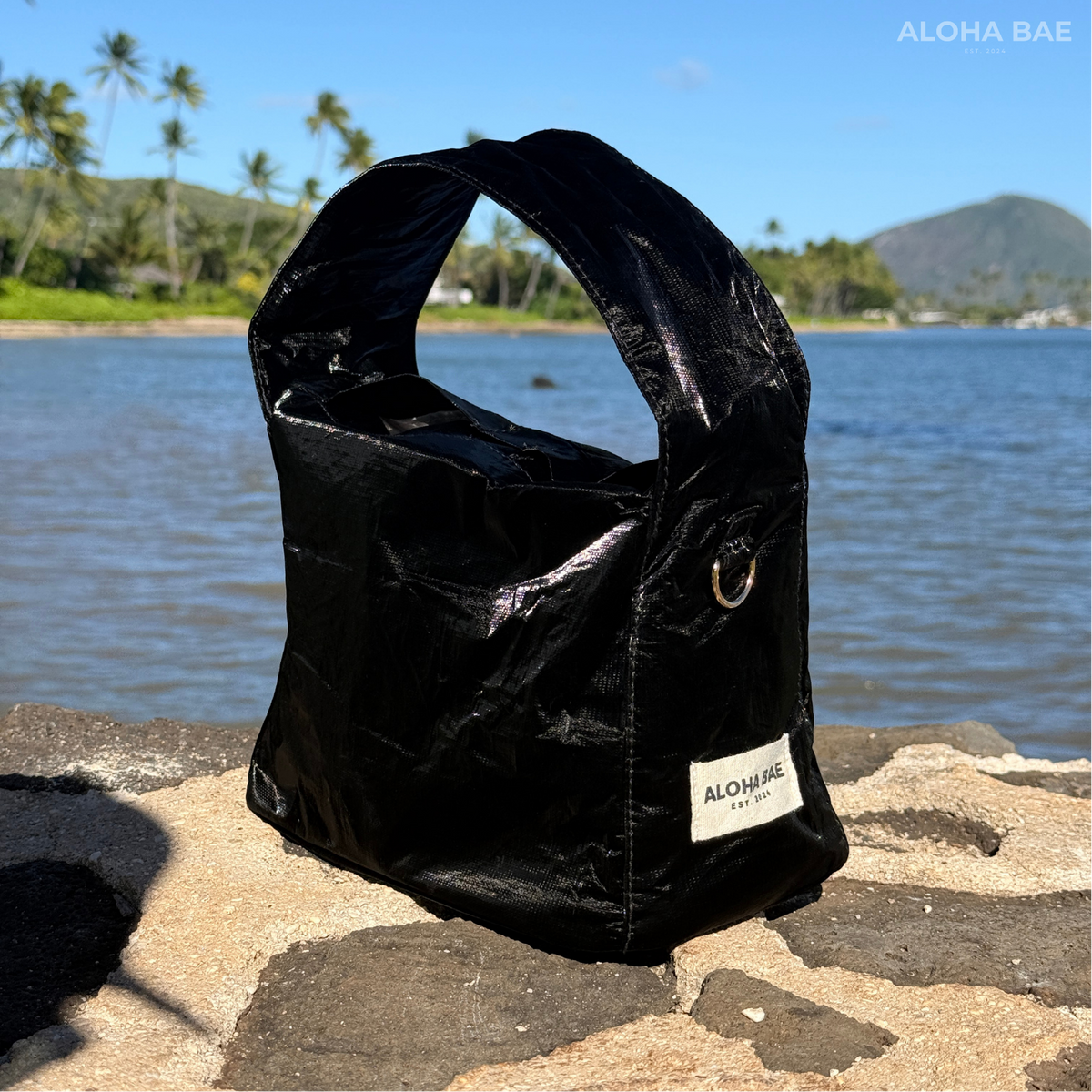 A black sheen hobo bag by alohabae featuring a slouchy style with a shoulder strap and subtle brand detailing.