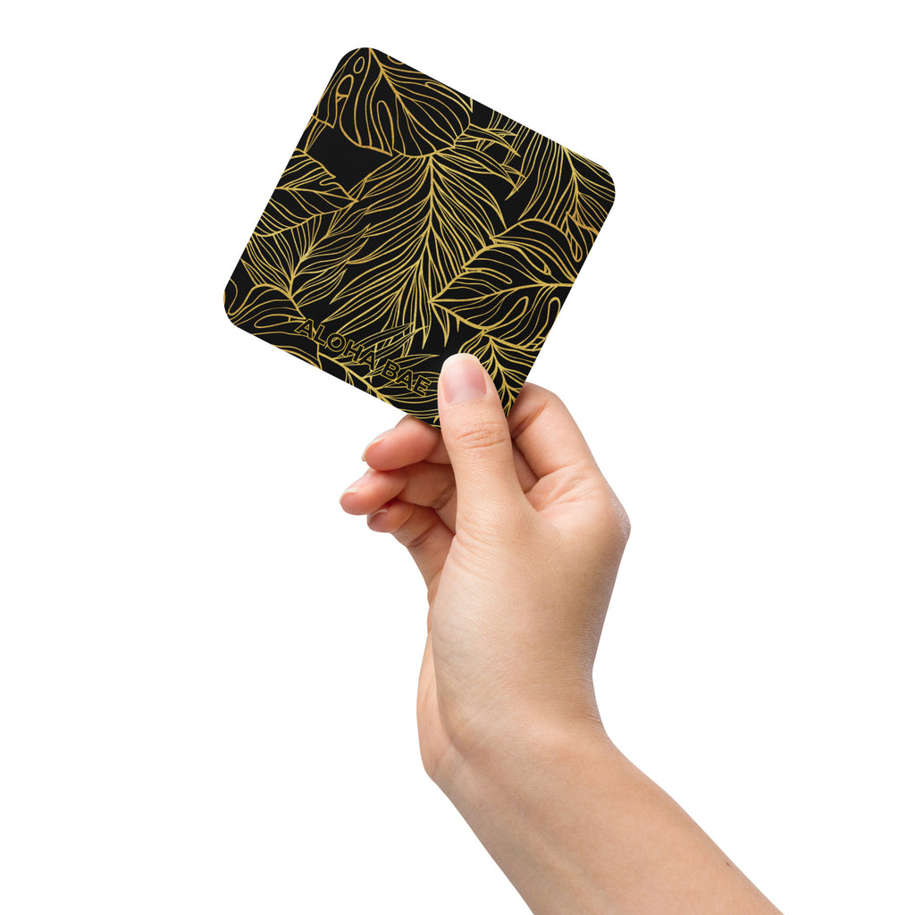 A black and gold monstera drink coaster with cork backing, featuring a tropical monstera leaf design.