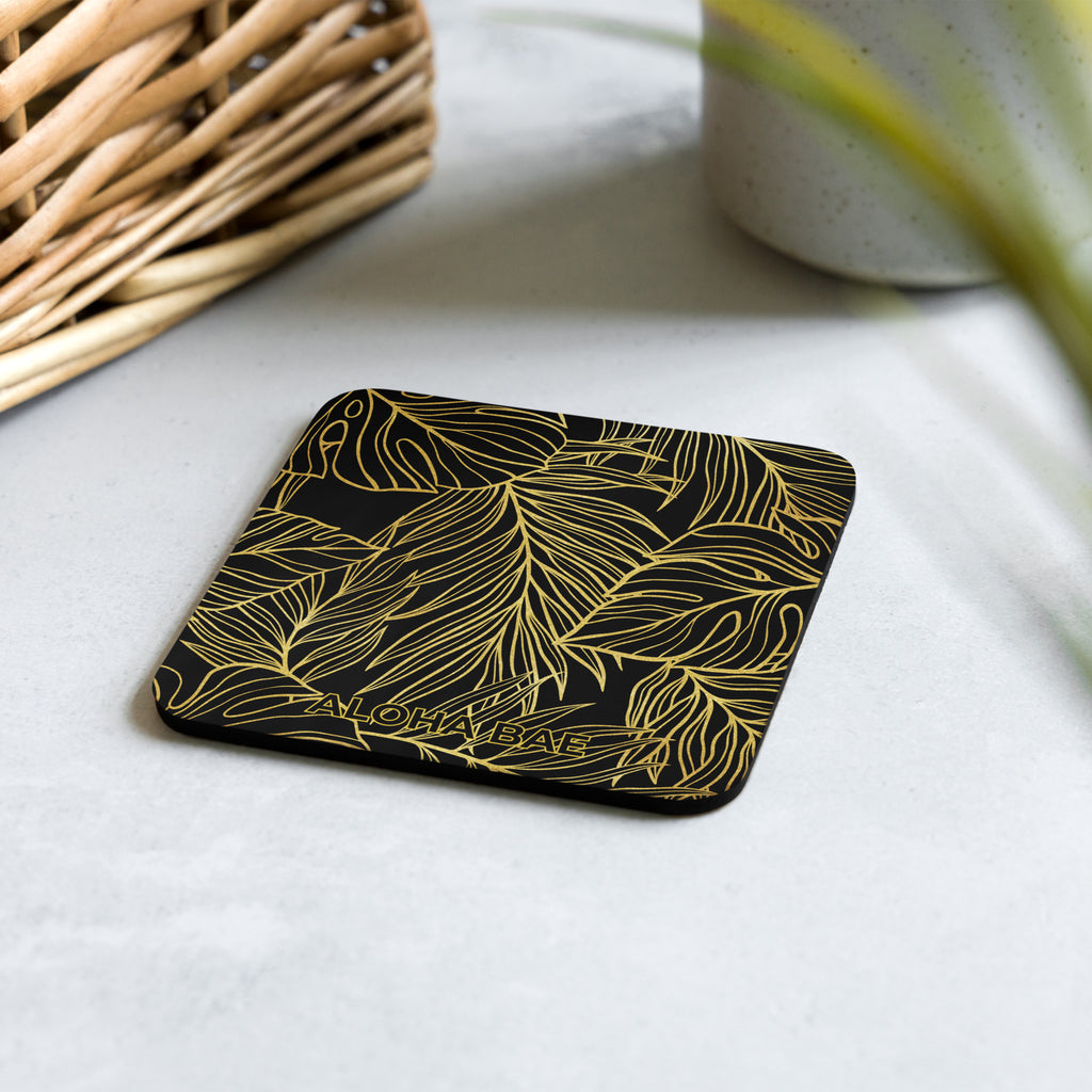 A black gold monstera cork-back drink coaster with a tropical leaf design, ideal for protecting surfaces from drinks.